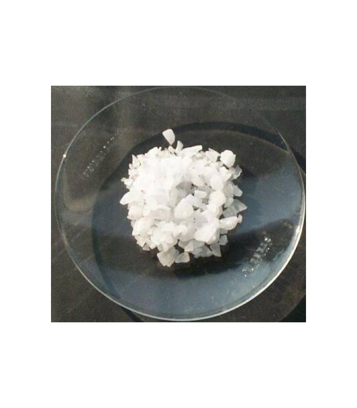 Cristales blancos de sulfato de aluminio de 1Kg, presentados en un plato de vidrio transparente sobre una superficie oscura.